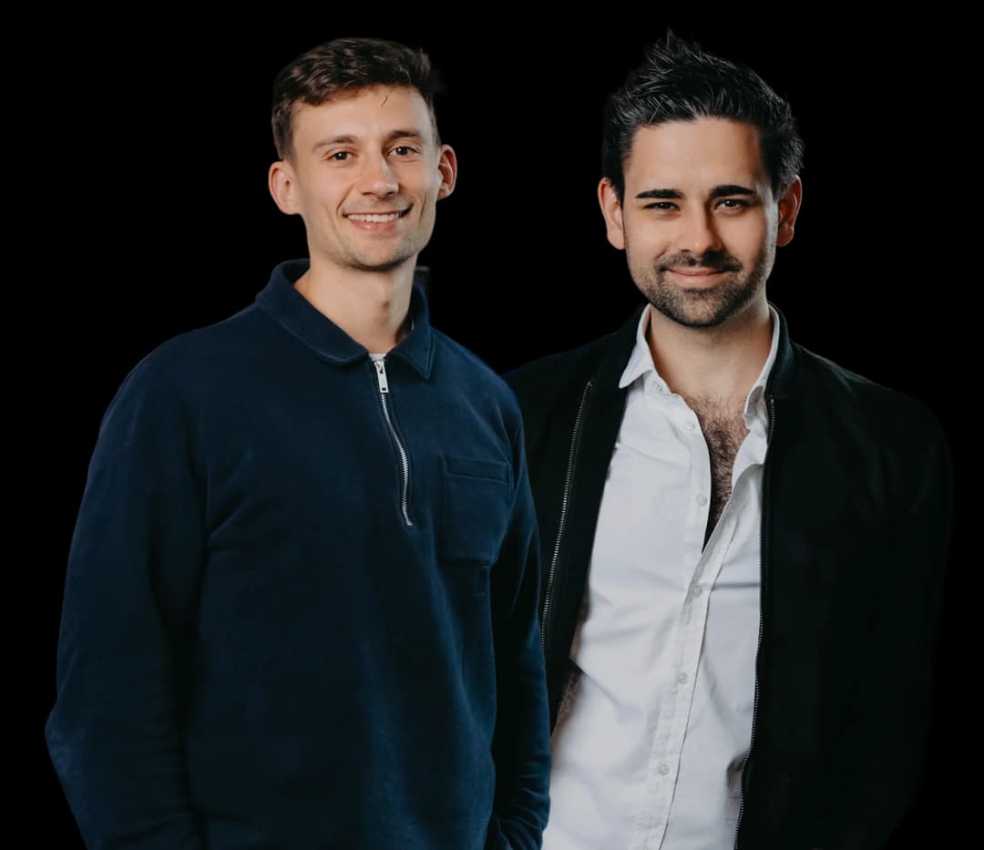 Two smiling men, one in a dark blue sweater, the other in a white shirt and black jacket.