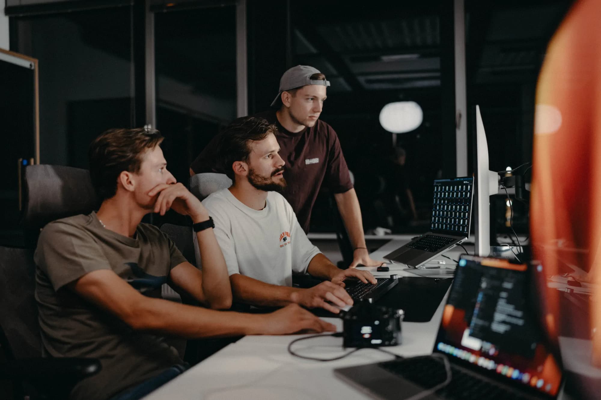 Three men working intently at computers in a dark office at night