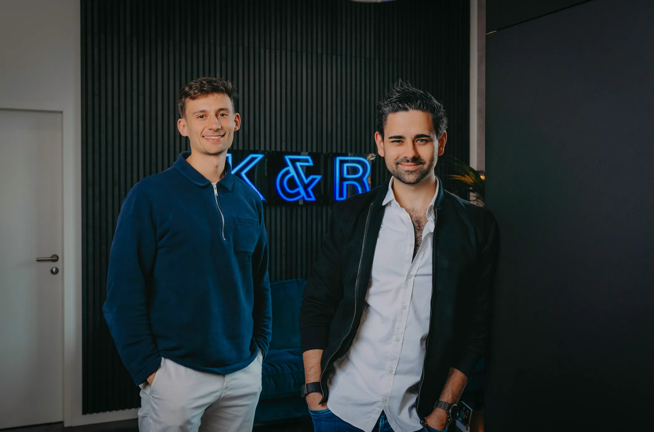 David Klein und Nicolas Rose vor schwarzer Wand mit leuchtendem K&R-Neonschild